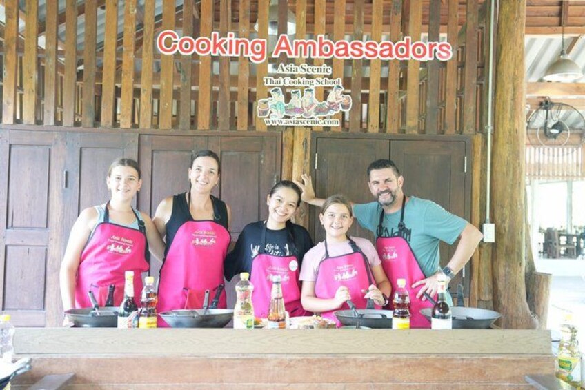 A group of people in aprons standing in front of a wooden structure with a sign that reads 'Cooking Ambassadors.' 4