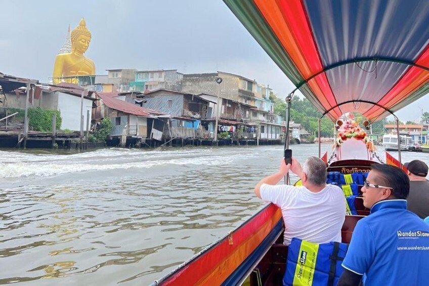 A boat with passengers, a large golden statue, and a river with buildings in the background. 4