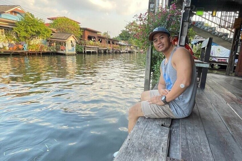 A person sitting on a wooden dock by a calm river, surrounded by houses and greenery. 5
