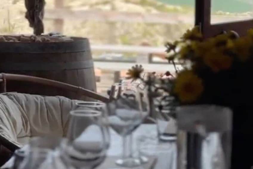 A dining table with wine glasses, a vase with flowers, and a rustic barrel. 5