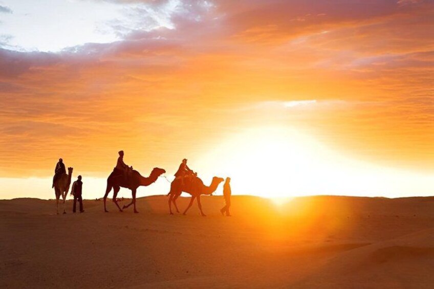 A desert landscape at sunset with people riding camels. 4