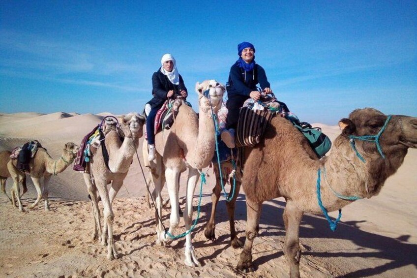 Three camels with riders in a desert landscape. 3