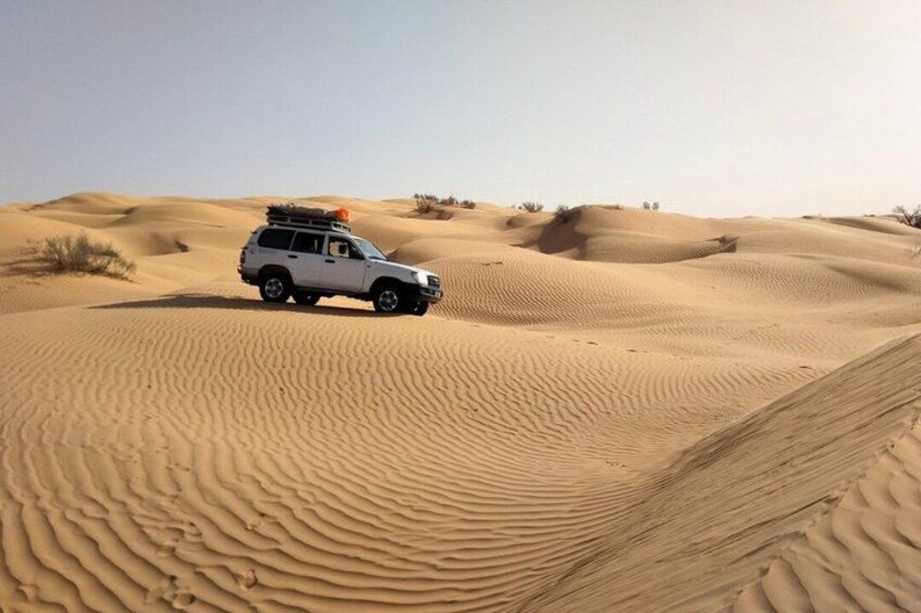 A white SUV on a sandy dune with ripples in the sand. 2
