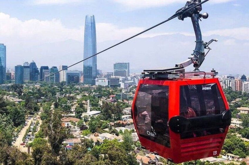 A red cable car with 'ROMA' written on it, suspended by a cable above a cityscape with buildings and greenery. 1