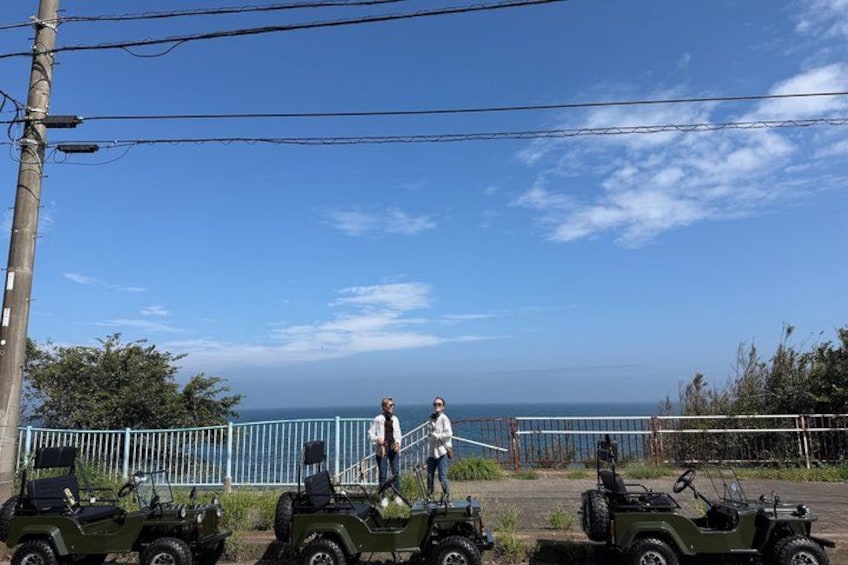 A coastal area with a clear sky, a fence, and several green jeeps parked along the roadside. 4