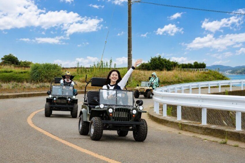 Three jeeps on a curvy road with a white guardrail, surrounded by greenery and a clear sky. 1