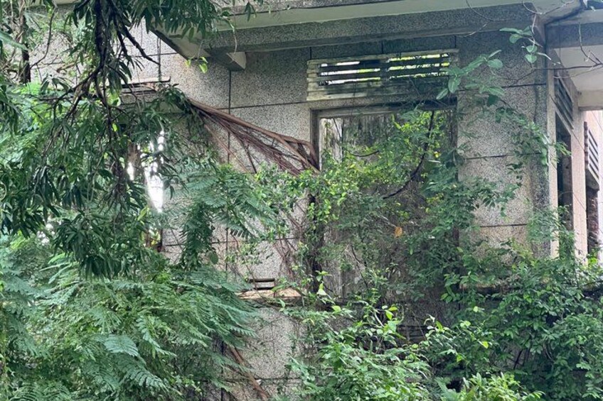 A stone building with overgrown vegetation, a metal staircase, and a partially visible window. 2