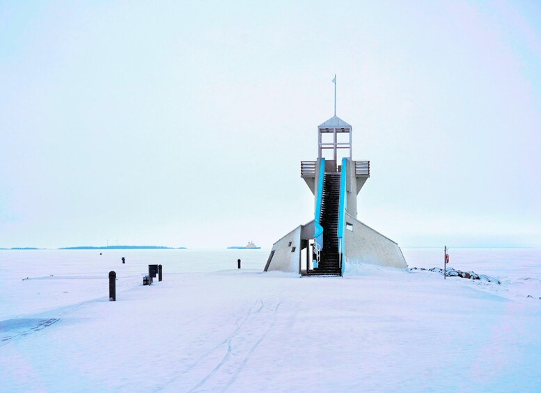 Un paysage enneigé, avec une haute tour étroite au centre, un navire lointain à l’horizon et un ciel dégagé. 3