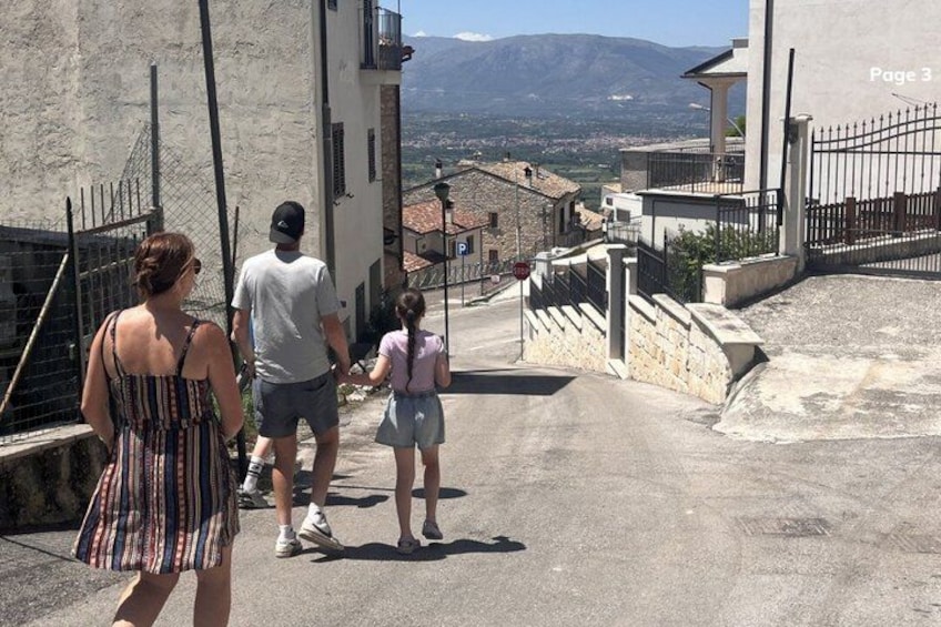 A family walking down a narrow street with stone buildings and a mountain in the background. 1