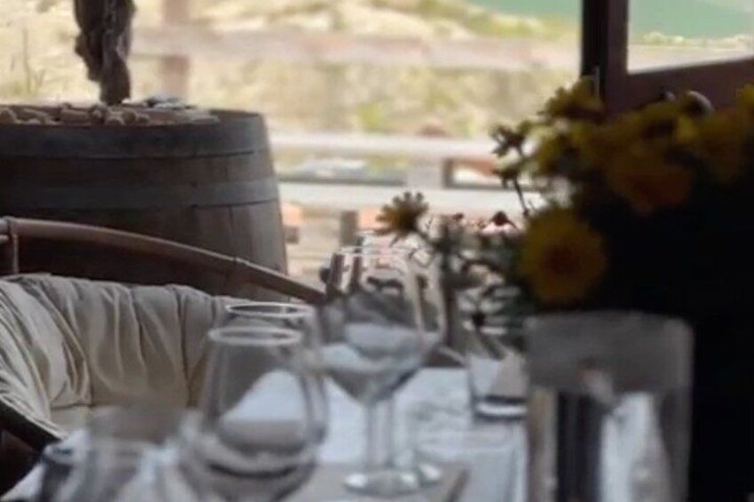 A dining table with wine glasses, a vase with flowers, and a rustic barrel. 2