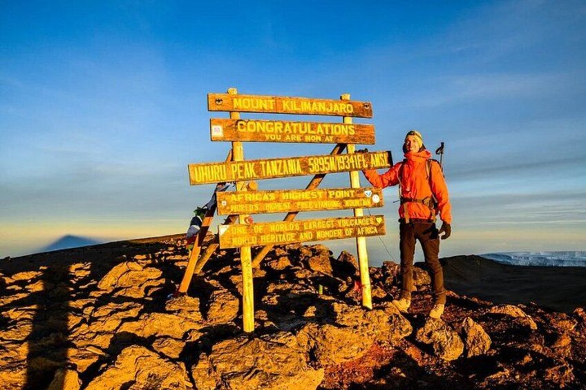 A person standing next to a signpost with multiple directional signs on a rocky terrain. 5