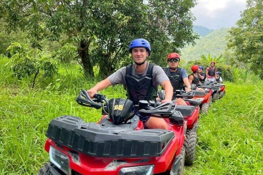 A group of people on red off-road vehicles in a lush green area with trees. 1