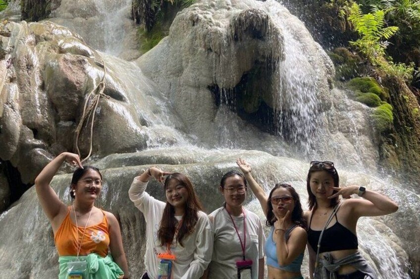 A group of people posing in front of a waterfall with large rocks. 2