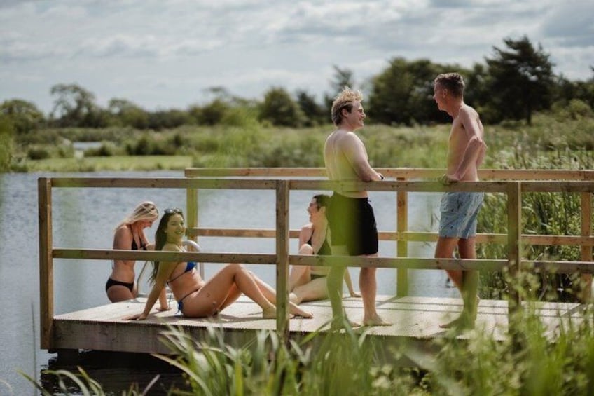 A group of people on a wooden dock by a body of water, with greenery in the background. 5