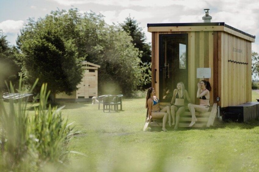 A wooden structure with a door, a bench, and a table in a grassy area with trees. 2