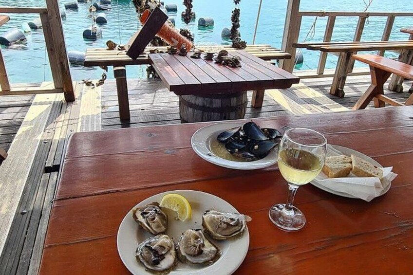 A wooden table with seafood dishes, a glass of white wine, and a view of the sea. 1