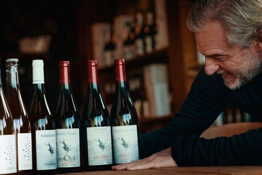 A person leaning over a table with several wine bottles. 5