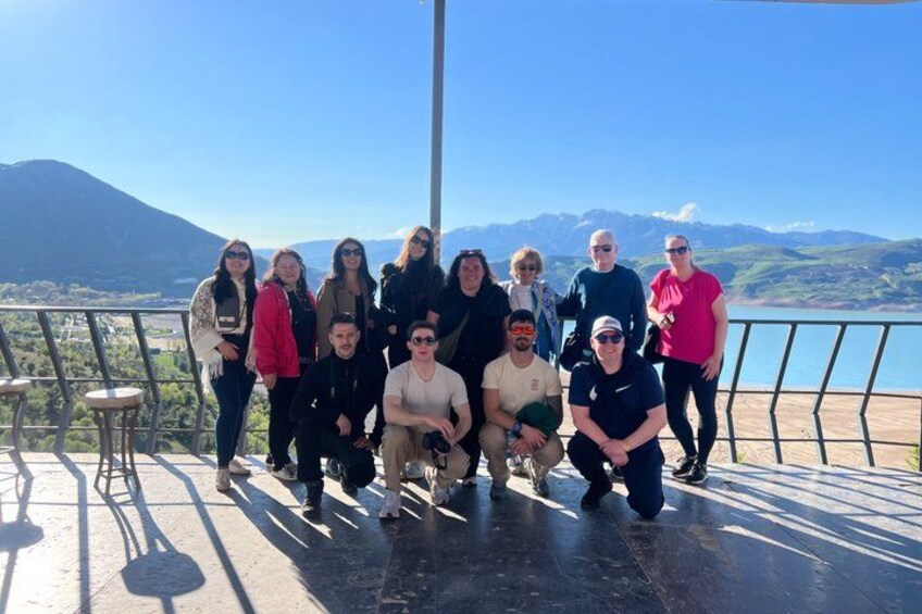 A group of people on a terrace with a mountain and lake in the background. 1