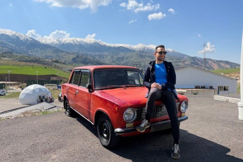 A vintage red car parked on a paved area with mountains in the background. 4