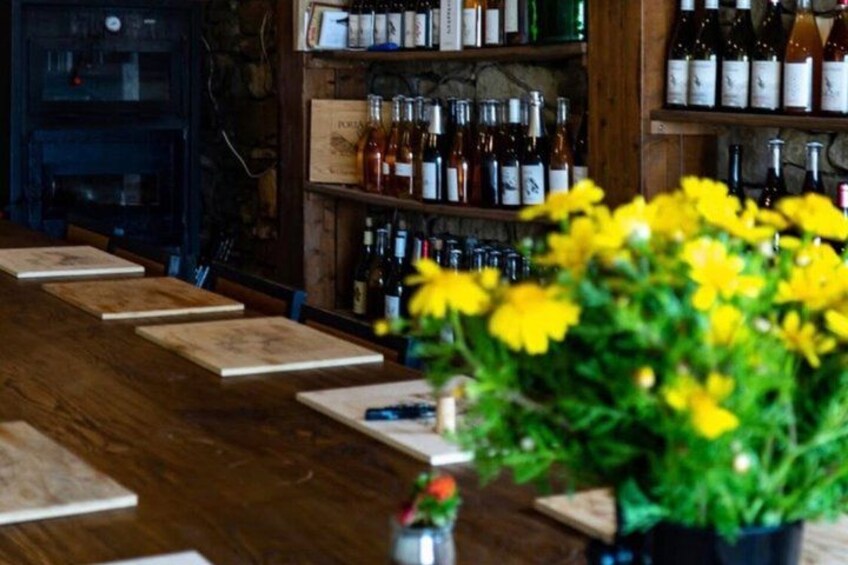 A bar with wooden shelves stocked with bottles, a wooden table with placemats, and a potted plant with yellow flowers. 3