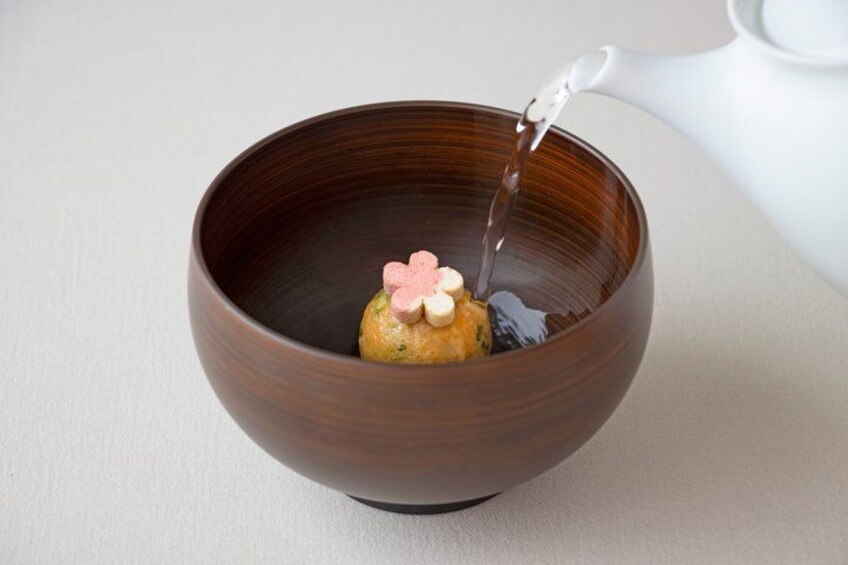 A brown ceramic bowl with a teapot pouring liquid into it. 4
