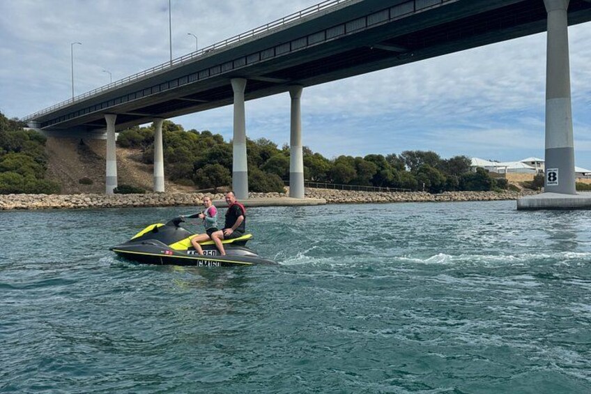 A person jet-skiing on a body of water with a bridge in the background. 1