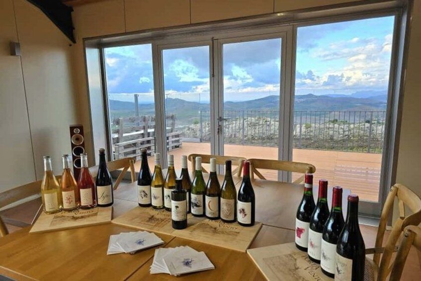 A table with wine bottles and menus in a room with large windows overlooking a landscape. 1