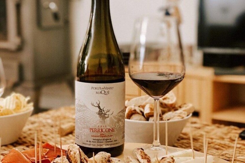 A bottle of wine with a label, a glass of red wine, and a bowl of snacks on a table. 3