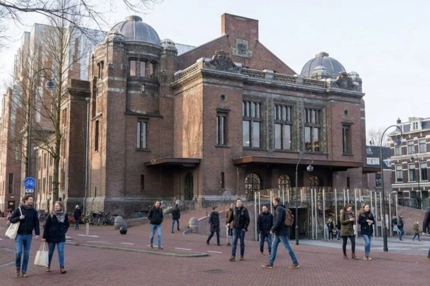 A historic building with large windows and a dome, surrounded by pedestrians on a paved area. 1
