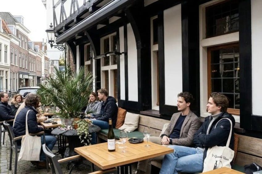 A group of people sitting at outdoor tables in a café with black and white striped architecture. 2