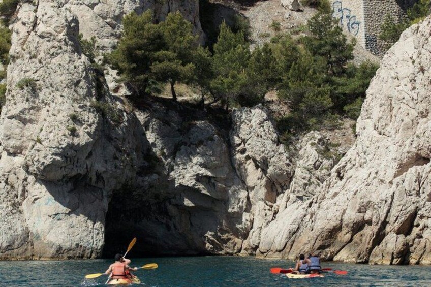 Kayakers in a cove with rocky cliffs and pine trees. 3
