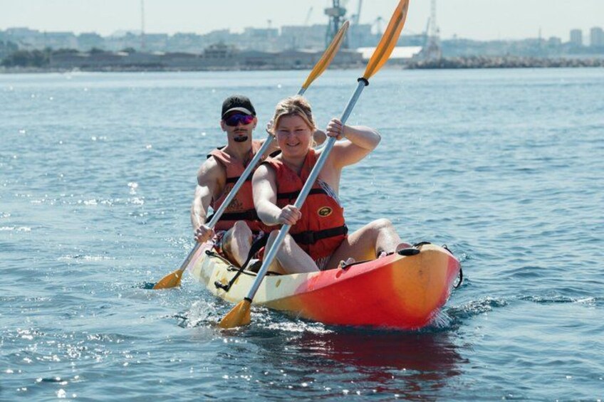 Two people kayaking on a calm body of water with a city skyline in the background. 4