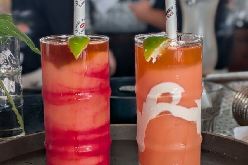 Two tall glasses of layered cocktails with lime garnishes on a bar counter. 2