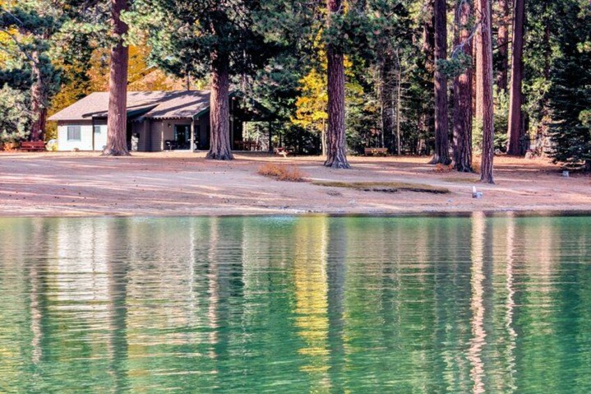 A lake with reflections, surrounded by tall trees and a building. 4