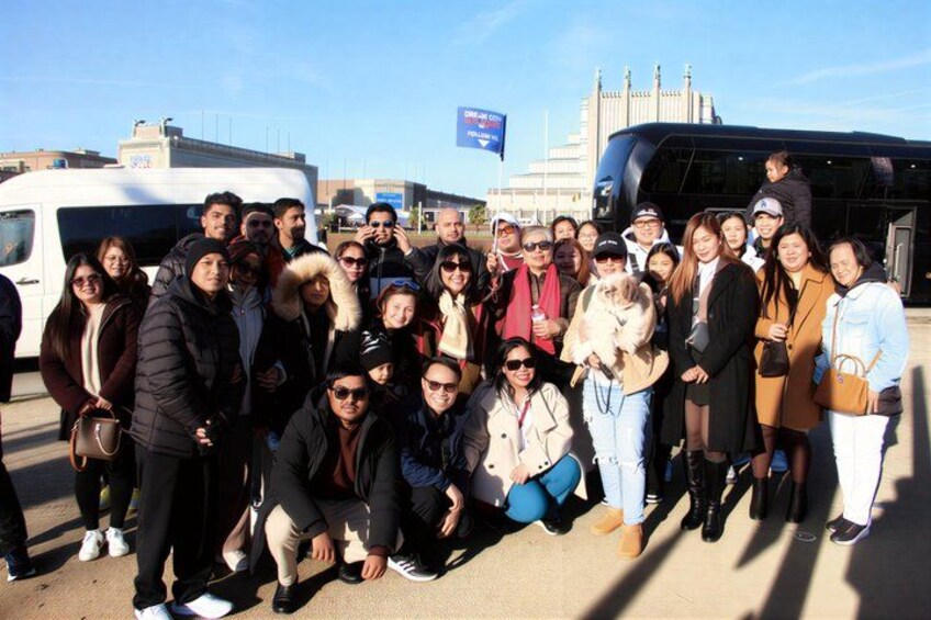 A group of people posing in front of a bus and a building with a blue flag. 4