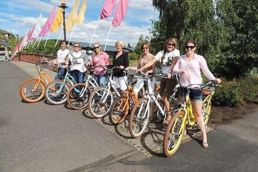 A group of people on bicycles lined up on a paved path with trees and flags in the background. 2