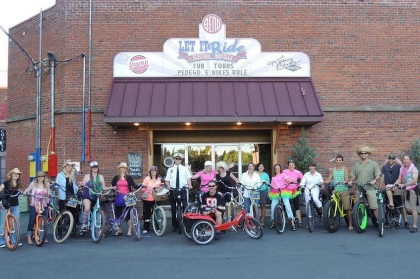 A group of people on bicycles in front of a building with a sign that reads 'Let It Ride Electric Bicycles Tours.' 1