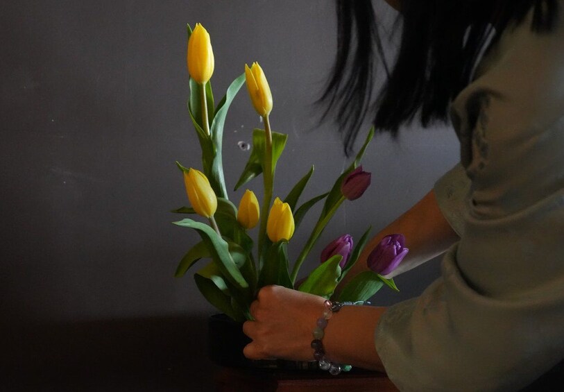 En person holder en vase med gule og lilla tulipaner. 3