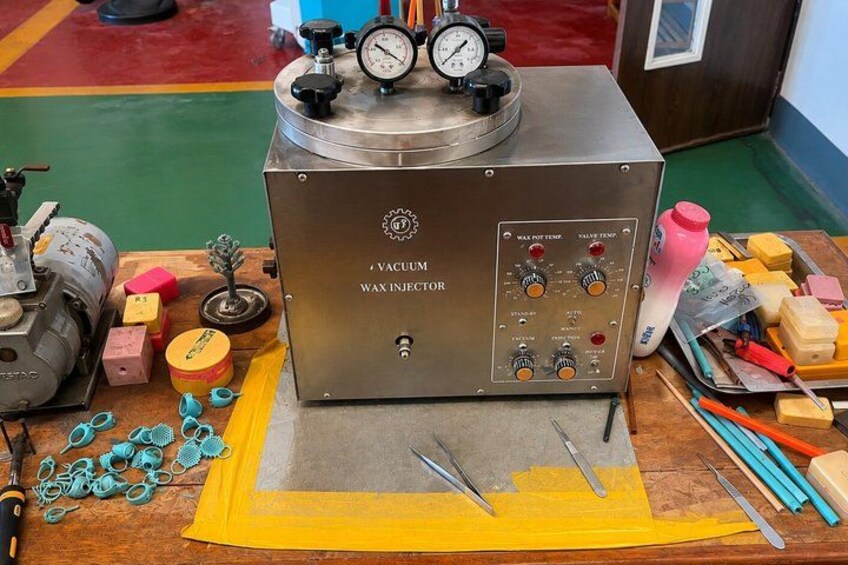 A vacuum wax injector with gauges, a yellow mat, and various tools on a wooden table. 4