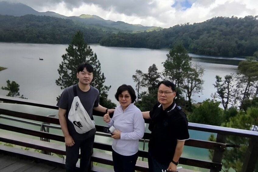 Three people standing on a bridge with a lake and mountains in the background. 2