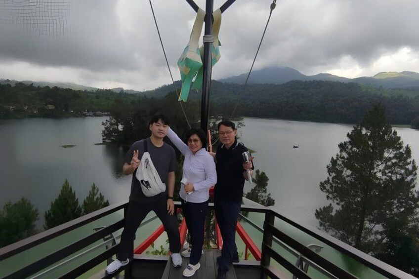 Three people on a cable car with a lake and mountains in the background. 5