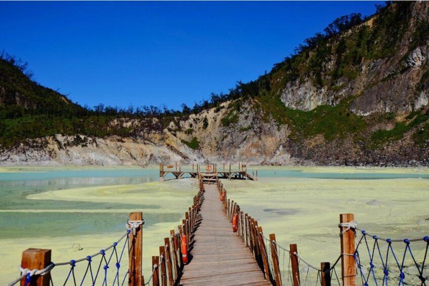 A wooden boardwalk leading to a dock over a calm, shallow body of water with clear turquoise color, surrounded by rocky cliffs and sparse vegetation. 1