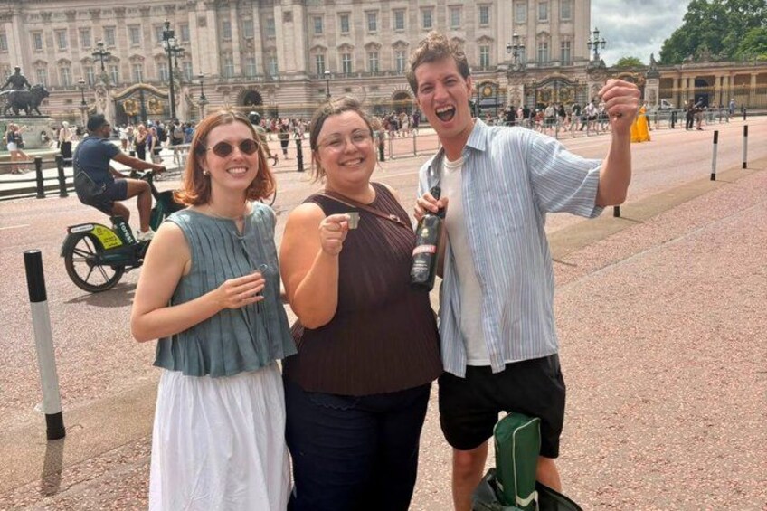 Three people posing in front of a historic building with a fountain and a statue in the background. 1