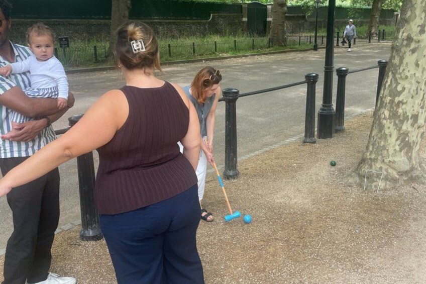 A person playing croquet with a blue ball on a dirt path. 5