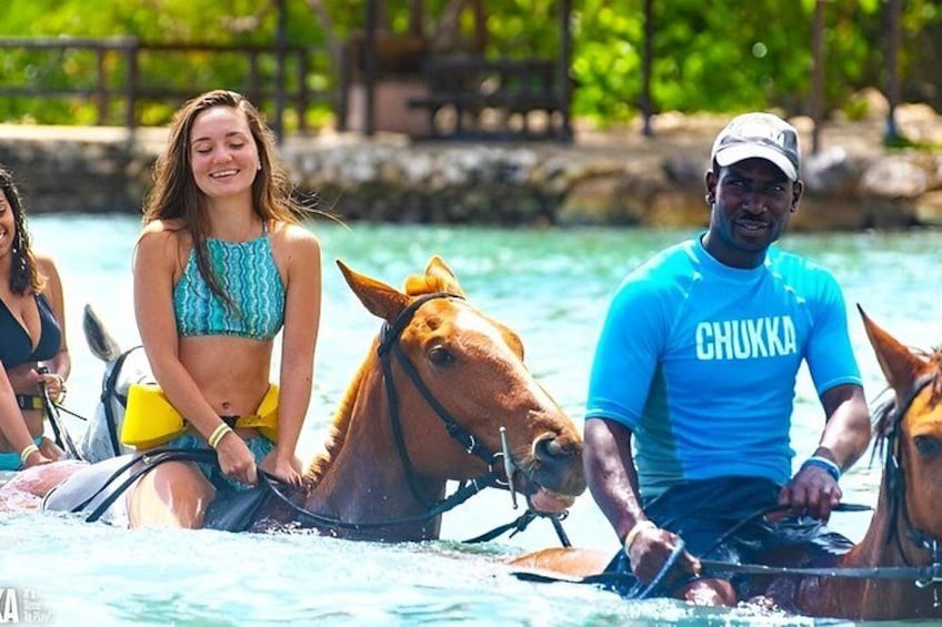 A person riding a horse in a body of water, with another person standing nearby. 1