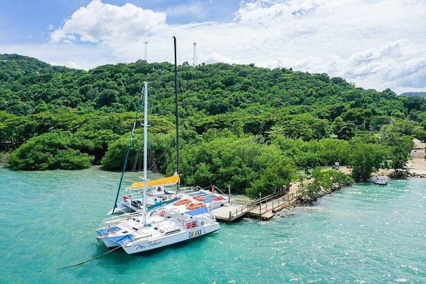 A sailboat docked at a pier with lush green hills in the background. 4