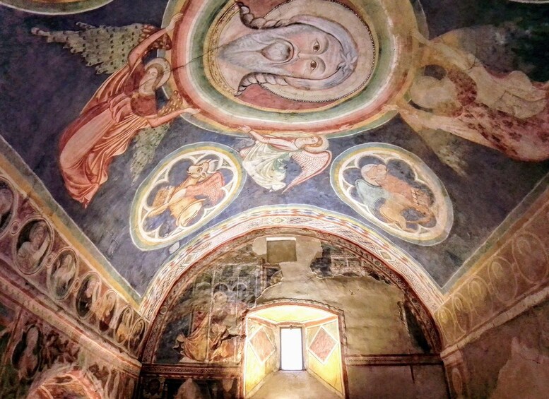 L’intérieur d’un bâtiment historique présente un plafond orné de fresques représentant des personnages et des scènes religieuses, une porte en arc de cercle et une petite fenêtre. 2