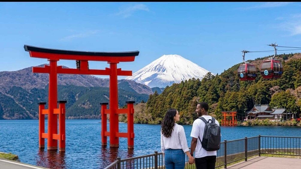Et par står ved en rød torii-port med et snedækket bjerg i baggrunden og en kabelbane i det fjerne. 1