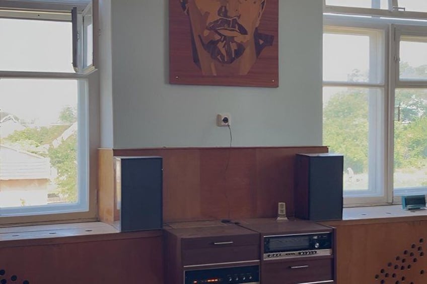 A room with a wooden desk, two speakers, and a painting on the wall. 5