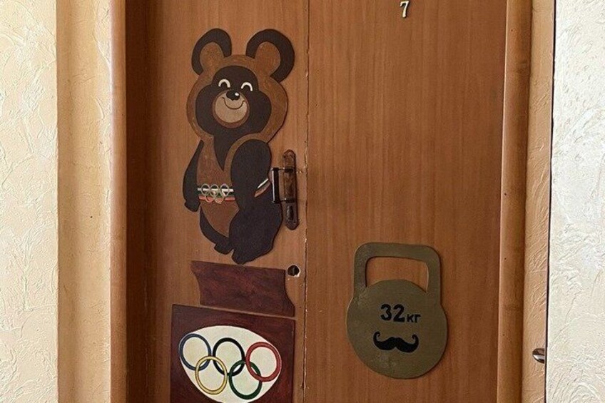 A wooden door with a bear cutout, Olympic rings, and a kettlebell symbol. 4